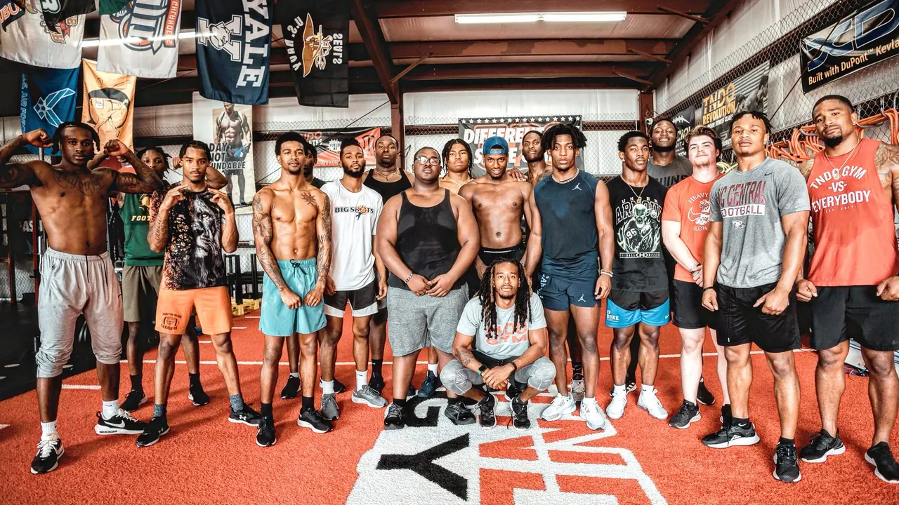 A line of TNDO athletes stands on the red turf behind the TNDO GYM floor logo.