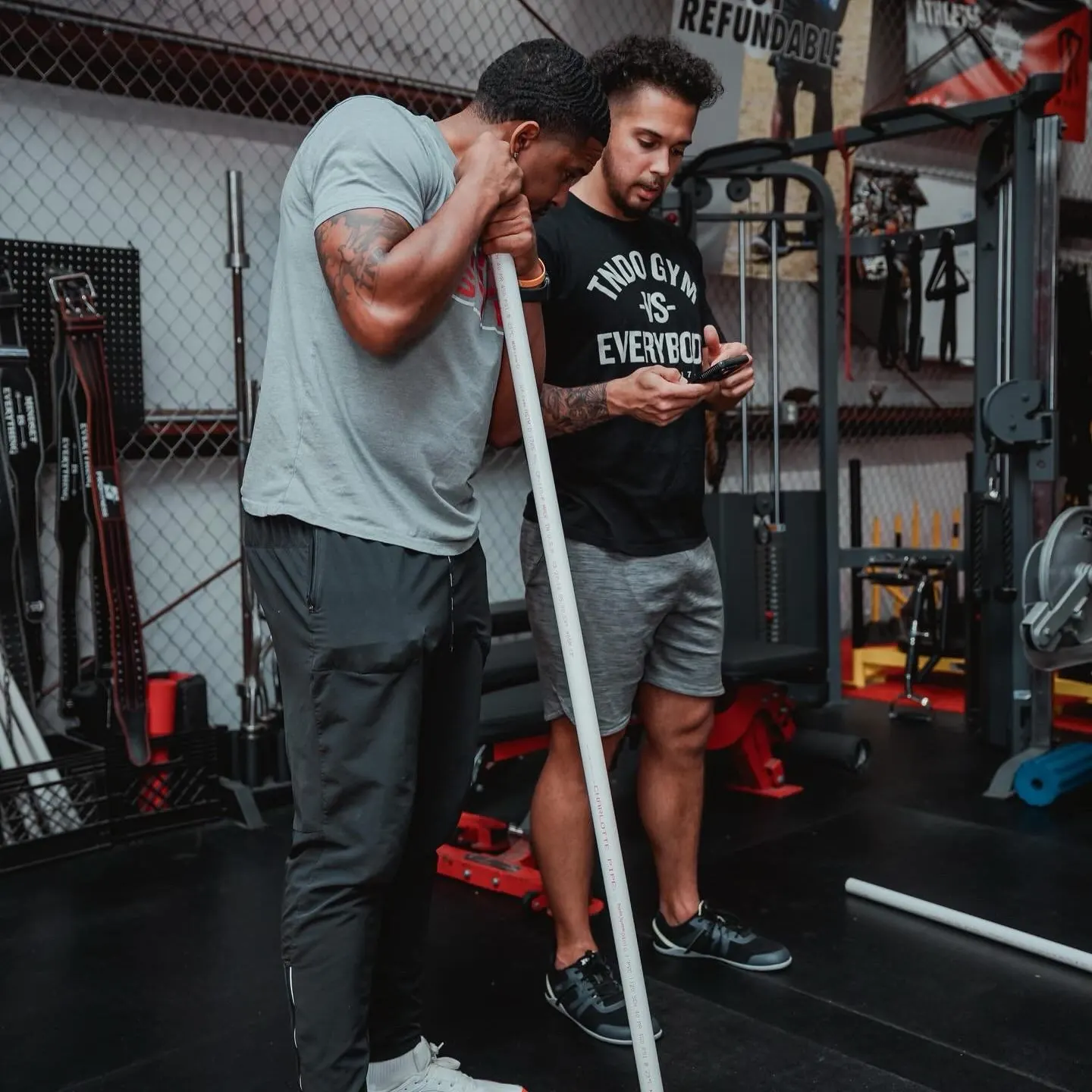 A TNDO coach reviews a rep on his phone with a member holding a training dowel