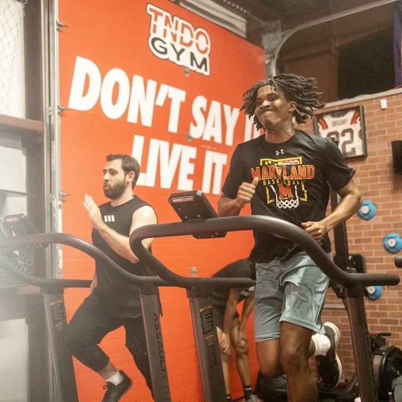Athletes sprint on curved treadmills in front of the Don't Say It, Live It wall