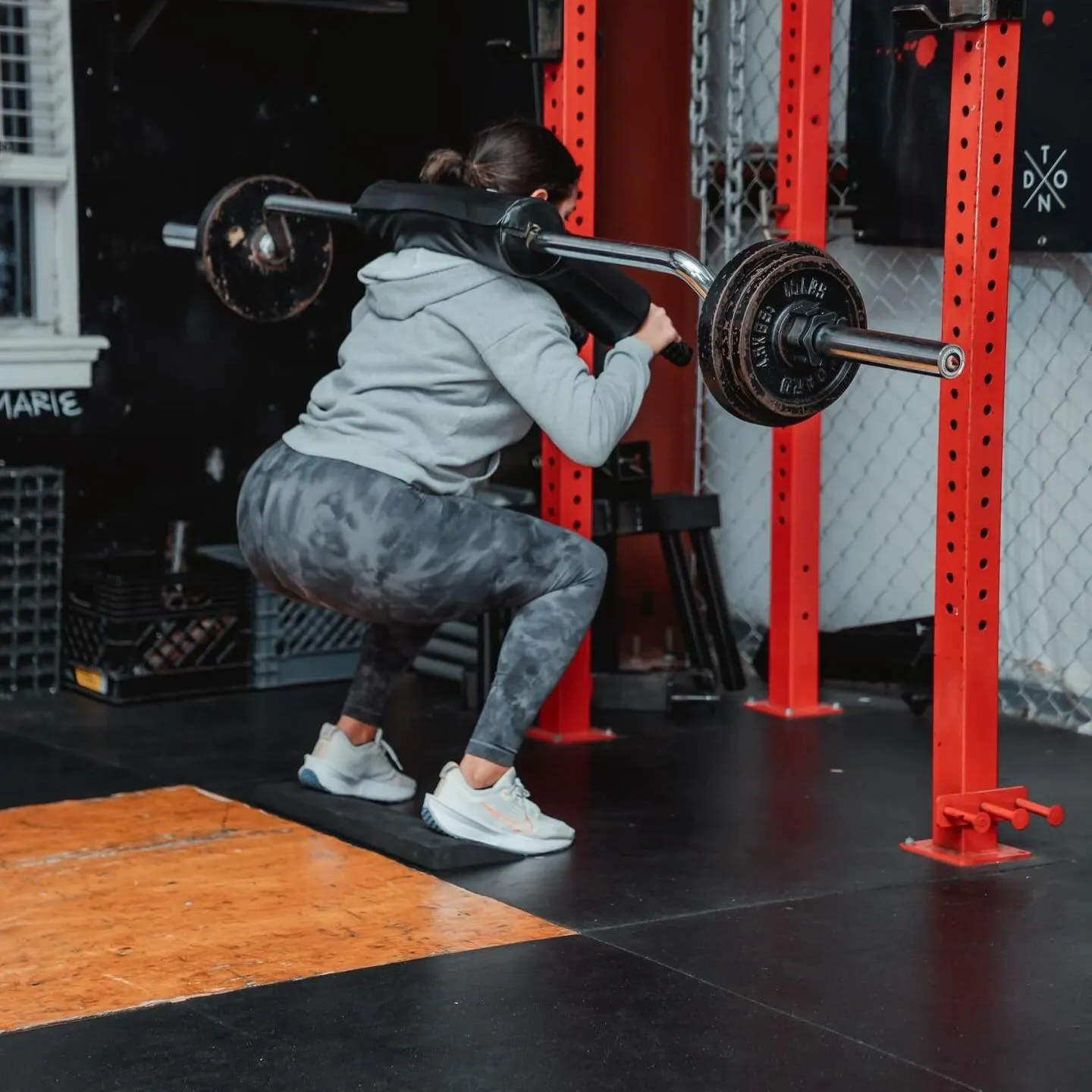 A member squats a safety bar inside TNDO's red squat racks