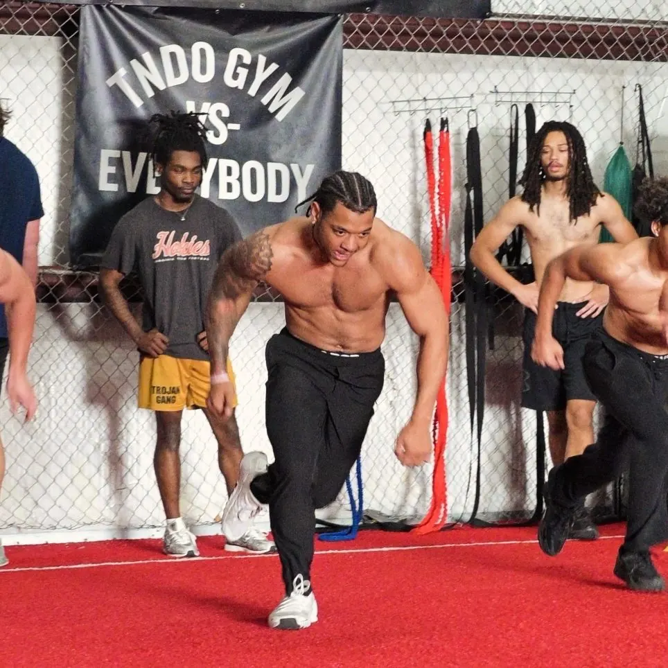 Athletes explode out of sprint starts on TNDO's red turf while teammates watch
